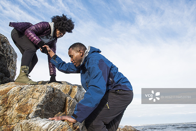 美国缅因州基特里，一名女子伸出手帮助男子爬上岩石图片素材