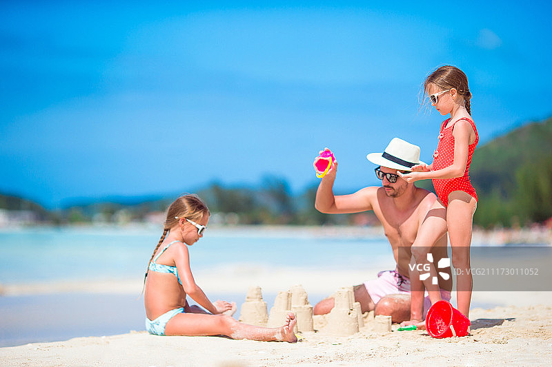父亲和两个女孩在沙滩上玩沙子图片素材