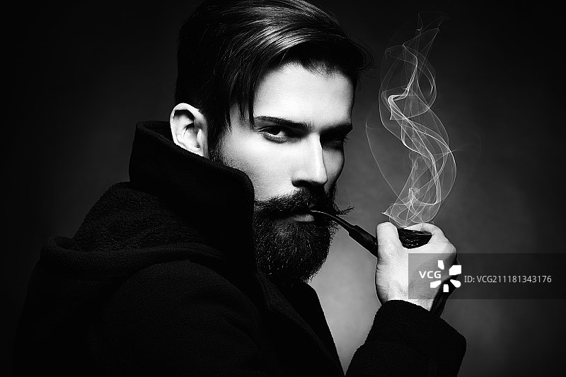 年轻漂亮的男人的黑色艺术肖像。那个年轻人抽烟斗。关闭了。黑白照片图片素材