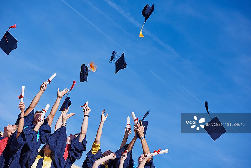 高中毕业生在蓝天上抛起帽子。图片素材