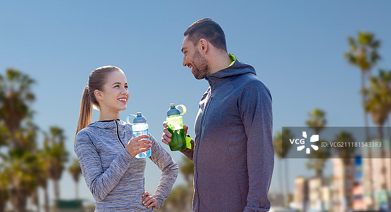 健身，运动和人的概念-微笑的夫妇与瓶装水在威尼斯海滩的背景在加利福尼亚。两个运动员和水在威尼斯海滩上。两个运动员和水在威尼斯海滩上图片素材