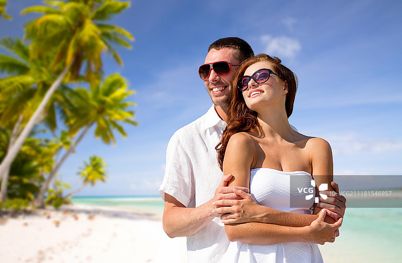 旅游，旅游和夏季度假概念-幸福的微笑夫妇在太阳镜在法国波利尼西亚的热带海滩背景。在热带海滩上，一对戴着太阳镜的幸福夫妇。在热带海滩上，一对戴着太阳镜的幸福夫妇图片素材