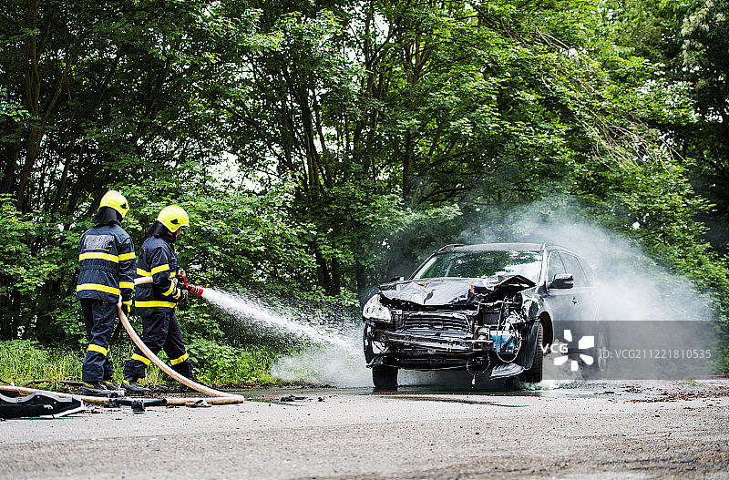 事故发生后，两名消防员正在扑灭一辆燃烧的汽车。图片素材
