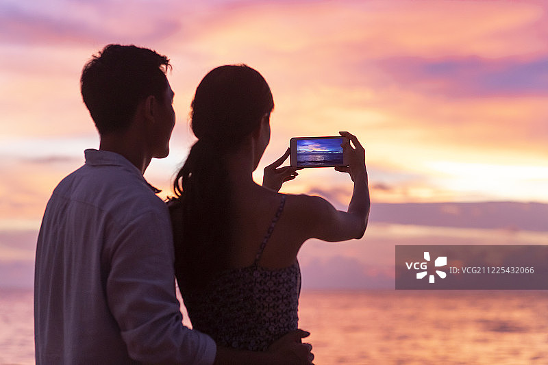 年轻情侣在海边使用手机拍摄海景图片素材