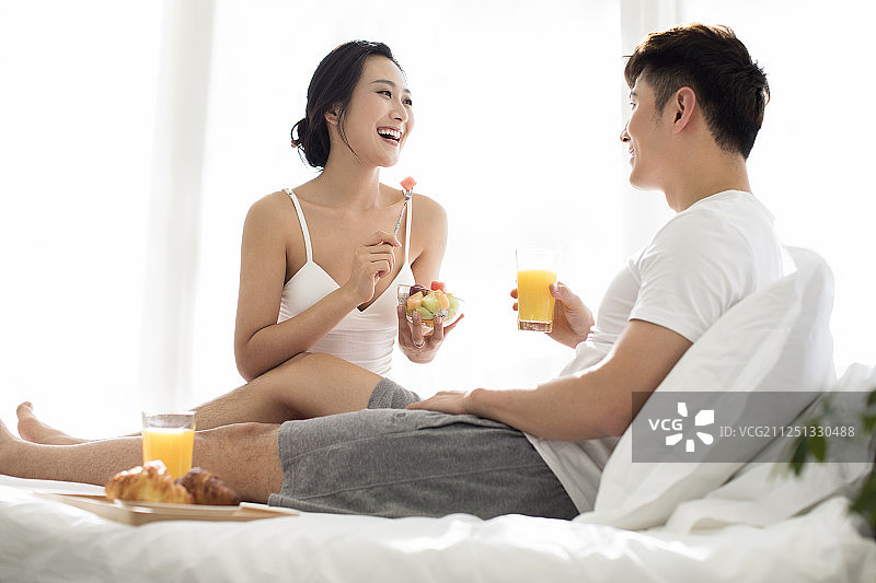快乐的年轻情侣在床上吃早餐图片素材
