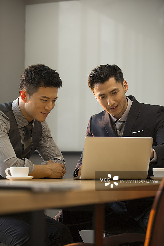 两个商务青年男子使用笔记本电脑在公司会议室讨论工作图片素材
