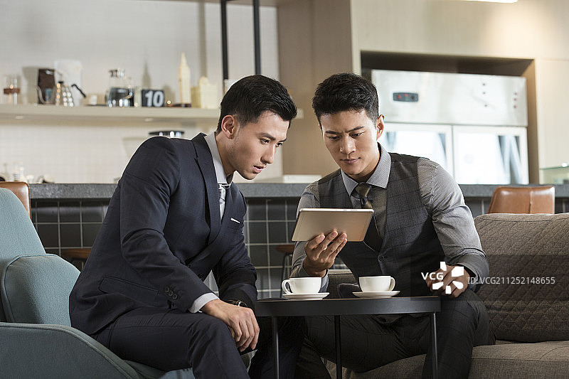 两个成功商务青年男子在酒店咖啡馆使用平板电脑沟通工作图片素材