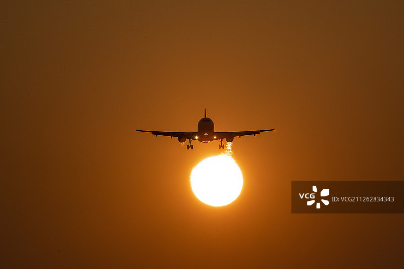 夕阳前半空中的飞机剪影图片素材