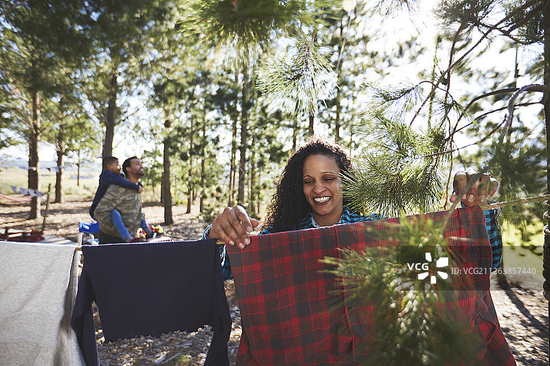 在树林里，一个微笑的女人在露营的晾衣绳上晾衣服图片素材