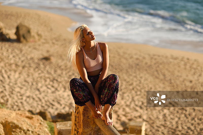 在西班牙安达卢西亚的加的斯，一名女子在美丽的海滩上欣赏日落。年轻女子坐在美丽的楼梯上，看着金色的大海。一个女人在美丽的海滩上欣赏日落图片素材