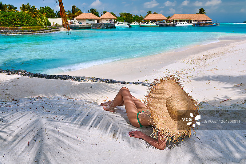 一个女人坐在沙滩上的棕榈树下。暑假在马尔代夫。图片素材