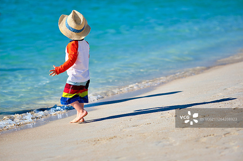 两岁的蹒跚学步的男孩戴着太阳帽走在海滩上图片素材