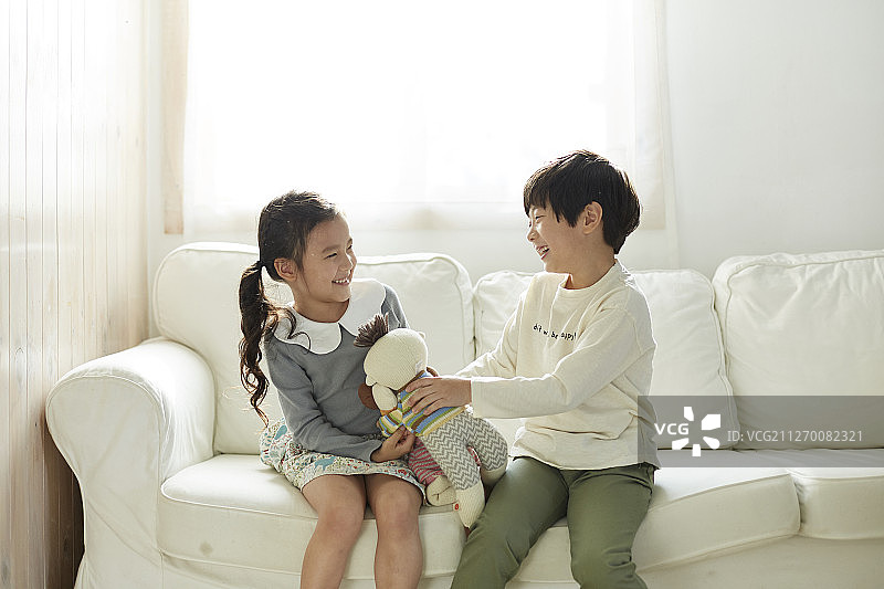 小女孩和小男孩坐在室内沙发上玩洋娃娃图片素材