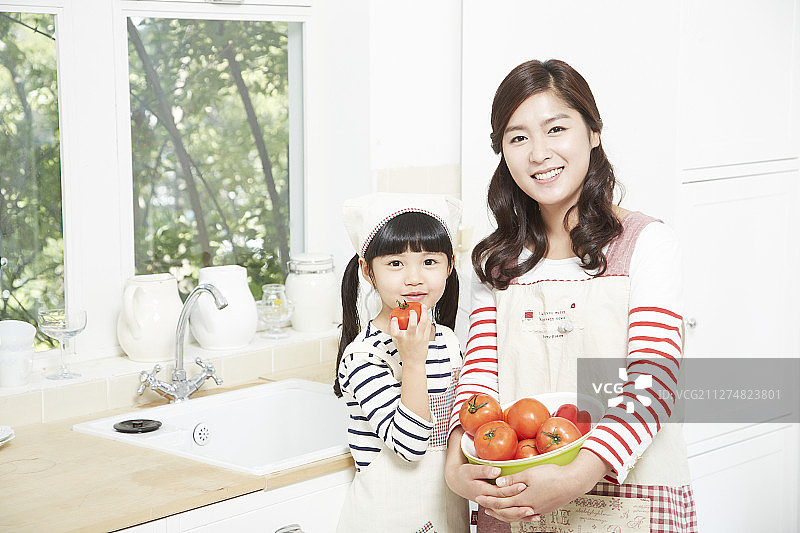 母亲和女儿在厨房拿着一碗西红柿的照片图片素材