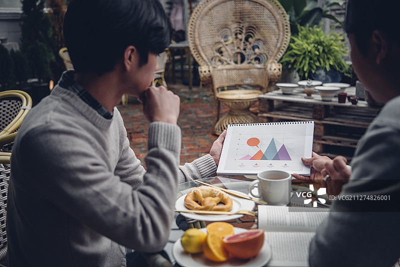 两个男人坐在桌子旁吃早午餐的照片在café户外一起看图表图片素材