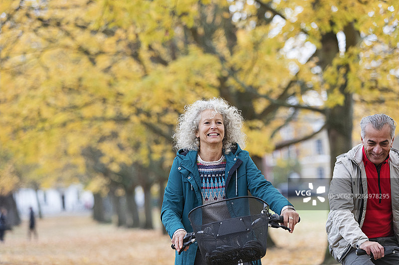 微笑着，无忧无虑的老年妇女自行车之间的树木在秋天的公园图片素材