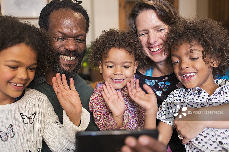 快乐的多民族家庭挥手，用智能手机视频聊天图片素材