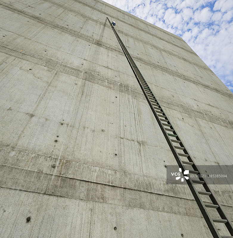远处人影爬上了靠在巨大工业建筑墙上的高高的梯子。3 d渲染。图片素材