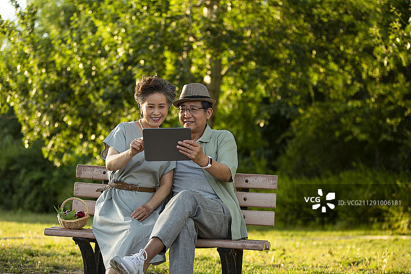 老年夫妻坐在户外公园长椅上休息使用平板电脑图片素材