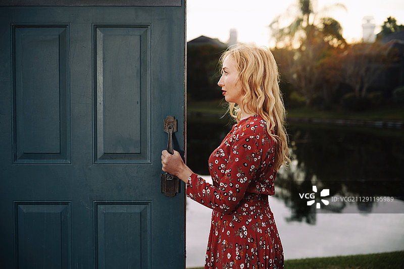 一个时尚的女人站在她家敞开的门旁边。非常适合书的封面图片素材