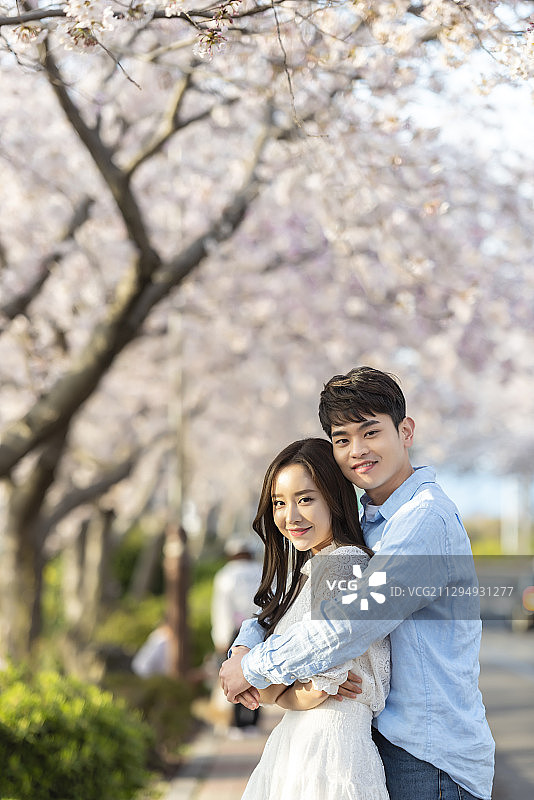 一对情侣站在樱花树下，男人从背后拥抱着女人图片素材