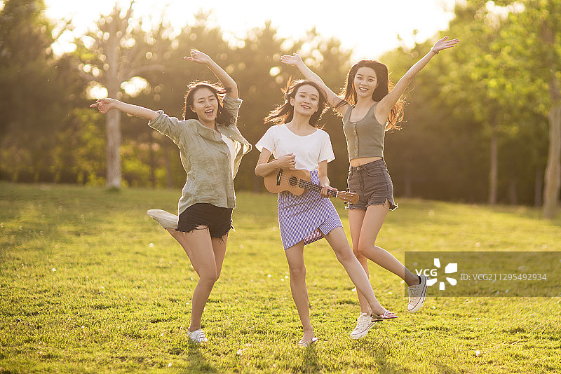 年轻闺蜜在草地上跳舞唱歌演奏音乐图片素材
