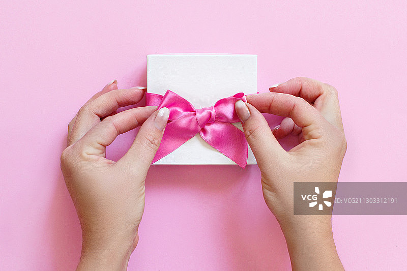 裁剪的手的女人拿着礼盒在粉红色的背景图片素材