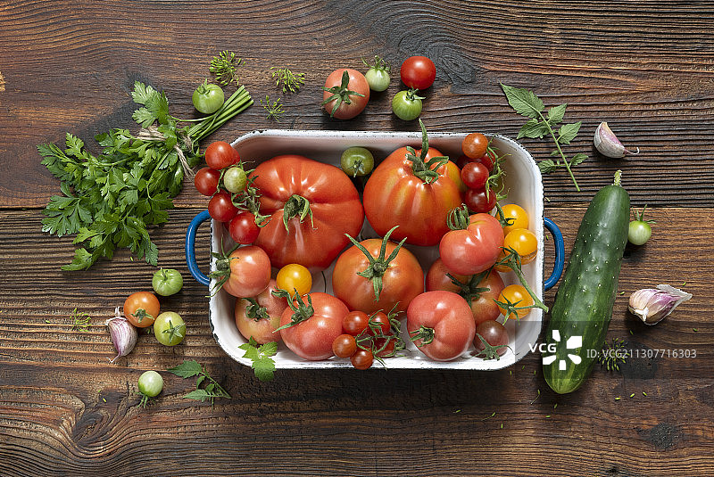 搪瓷容器里装着各种各样的西红柿，旁边是黄瓜、香草和大蒜图片素材