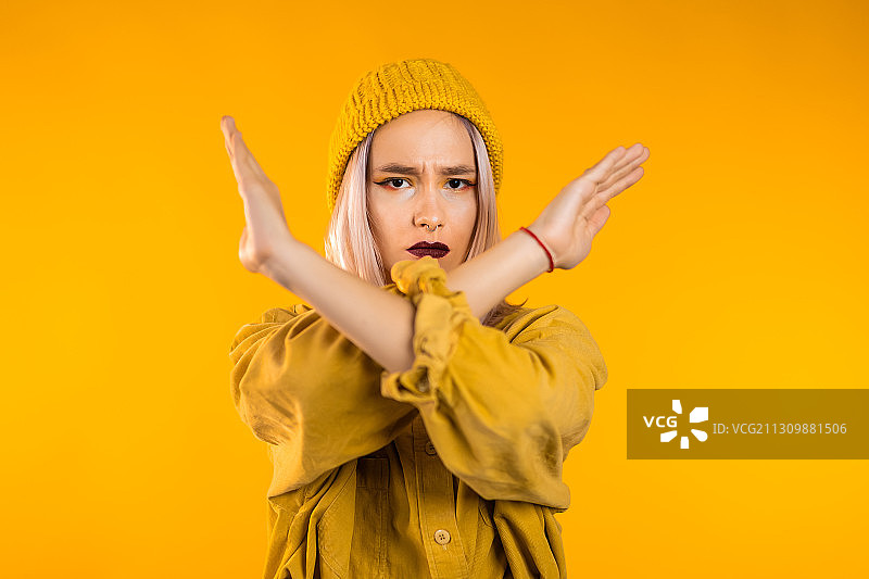年轻女子的肖像穿着黄色的衣服，在黄色的背景下，用手臂做x图片素材