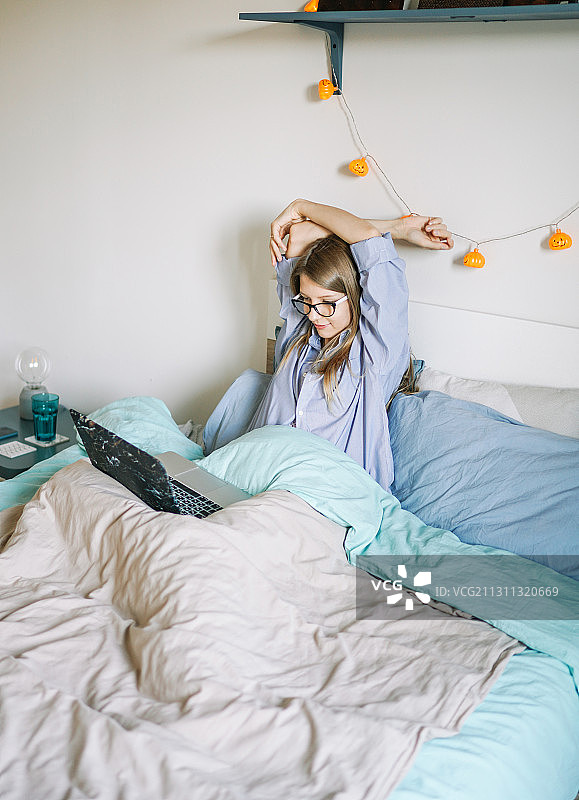 白人妇女在舒适的床上用笔记本电脑工作，西班牙图片素材
