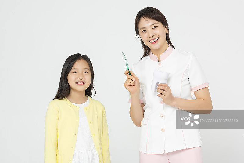 护士拿着牙齿模型和牙刷旁边的女孩站在白色的背景上图片素材
