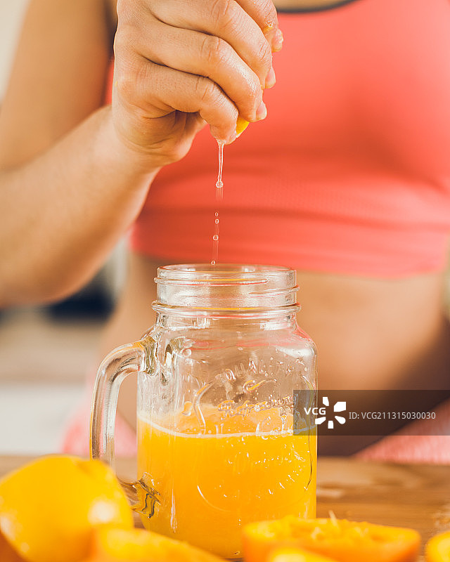 德国，一名女子正把新鲜的橙汁挤进玻璃杯图片素材