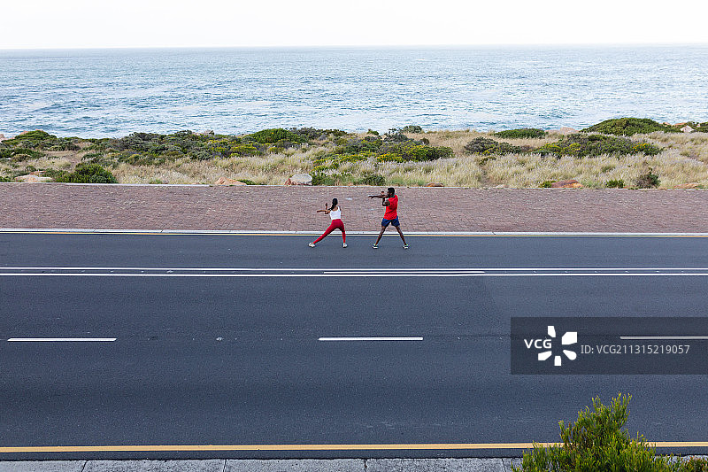 合身的非裔美国夫妇穿着运动服伸展在海岸公路上图片素材