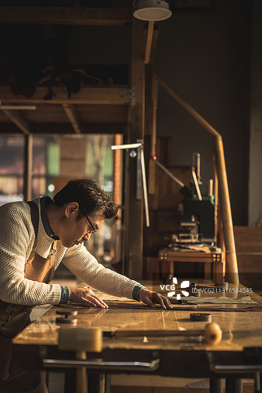 一个成熟的男人坐在车间的桌子旁制作皮革工艺品图片素材