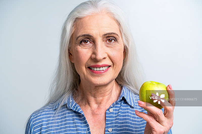 一个微笑的老妇人在灰色的背景下拿着苹果的肖像图片素材