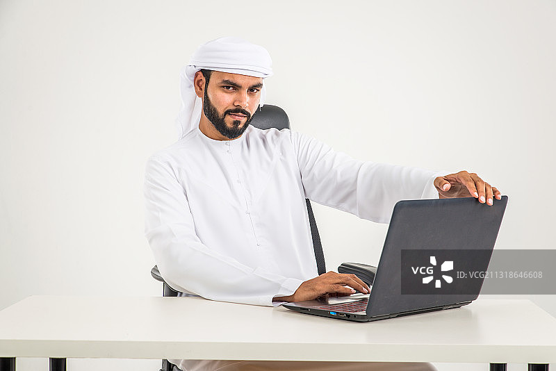 年轻的阿拉伯商人坐在白色背景下的办公桌前图片素材
