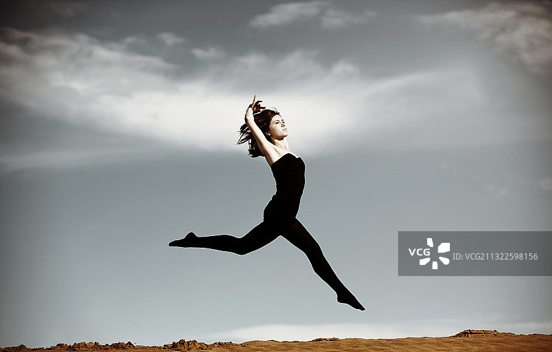 穿着黑色紧身衣的女人在沙漠里蹦蹦跳跳图片素材