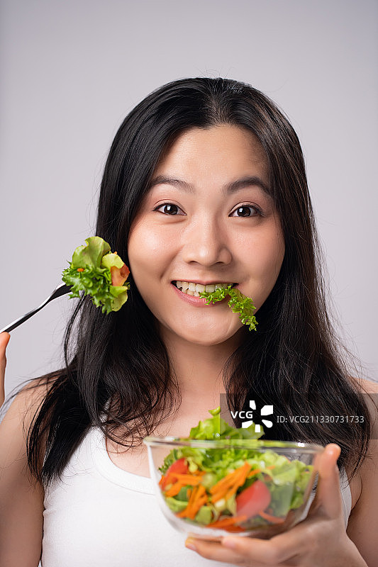 微笑的年轻女子吃沙拉的肖像白色的背景图片素材