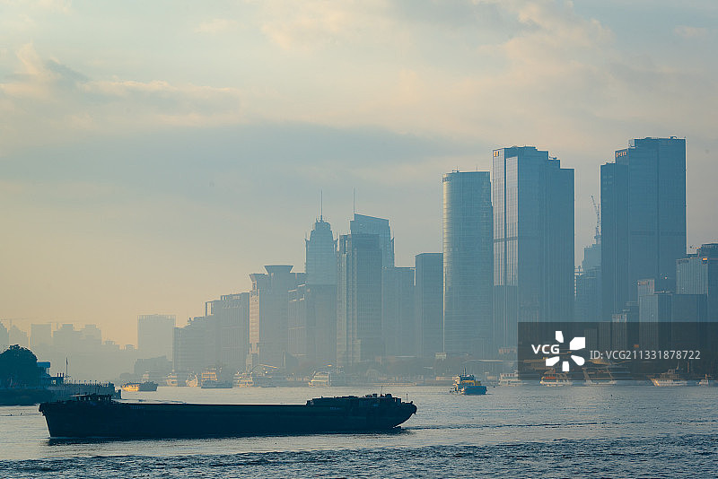 日出时分的外滩摩天大楼群，宽阔的黄浦江江面上一艘货轮驶过图片素材