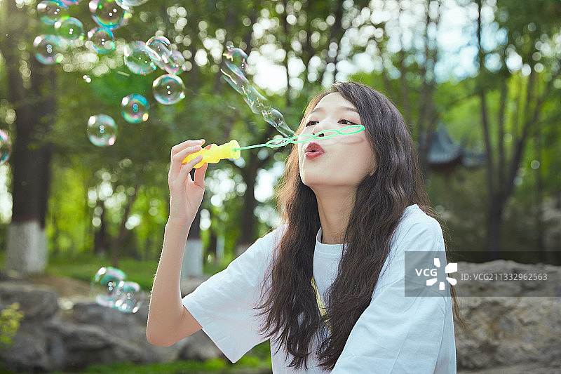 户外公园里玩吹泡泡的可爱亚洲少女图片素材