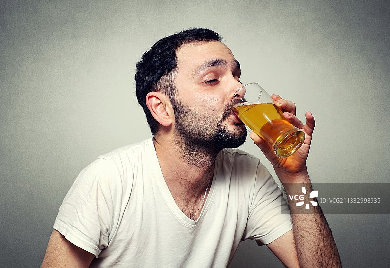 在灰色背景下喝啤酒的男人图片素材
