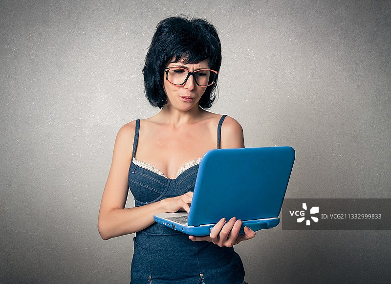一个女人站在灰色背景下使用笔记本电脑图片素材