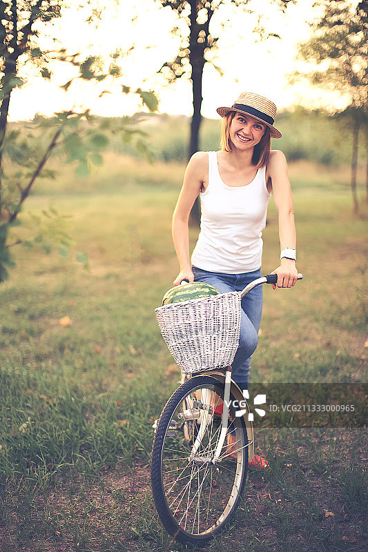 美丽微笑的女孩戴着草帽和自行车在公园图片素材