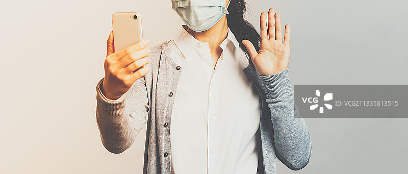 女医生戴着外科口罩，对着墙壁用手机图片素材