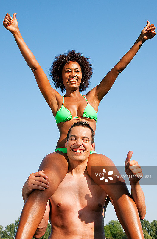 相爱的夫妇——穿比基尼的有色人种女人坐在她的男人身上?�6�4蓝天下的肩膀——夏日和乐趣图片素材