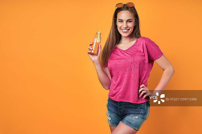 微笑的年轻女子的肖像拿着橙汁，而站在橙色的背景图片素材