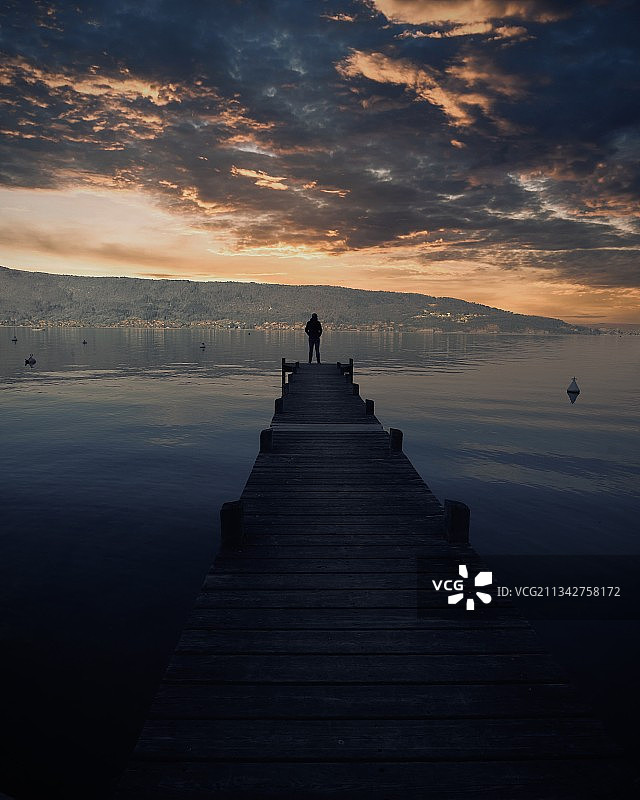 日落时分，一个人站在海上的码头上的剪影图片素材