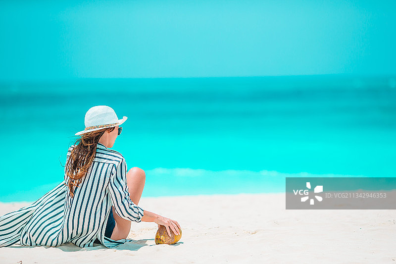 背面的女人坐在海滩上对着蓝色的天空图片素材