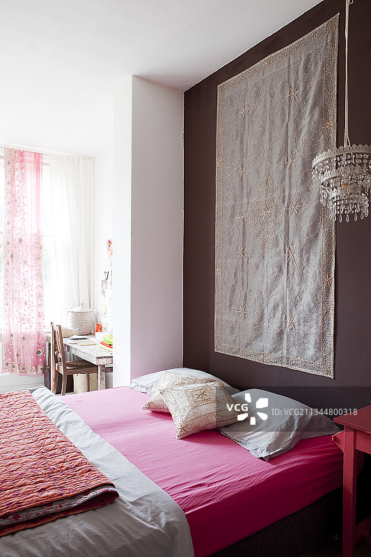 卧室里的一面挂着挂毯的深色墙壁前放着一张粉色床单的床垫图片素材
