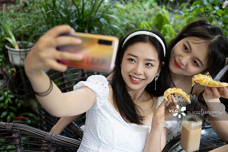 两个女孩边吃边用手机拍照图片素材